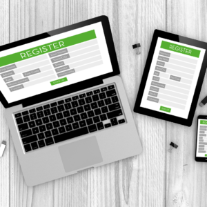 A laptop, tablet and phone are on a table. Each of them are displaying a registration form. The questions on each form are not legible.