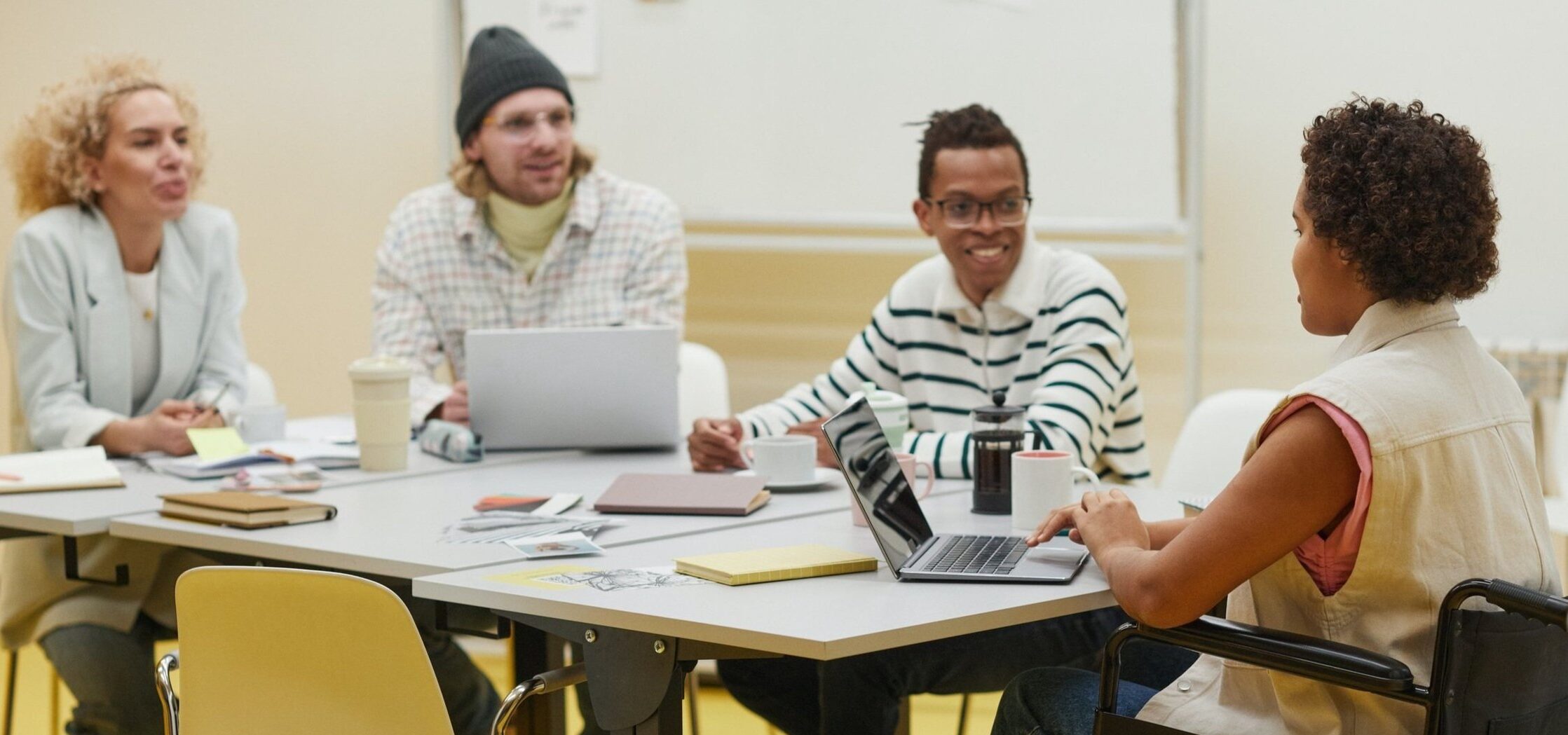 Diverse group of coworkers planning an event. From right to left: a blond white female, a blonde white male, a Black male with glasses, and a Black female seated in a wheelchair.