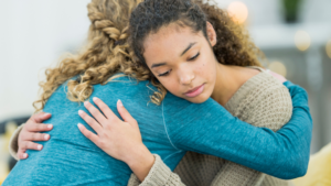 Young Latina with curly hair hugging another woman in a teal sweater