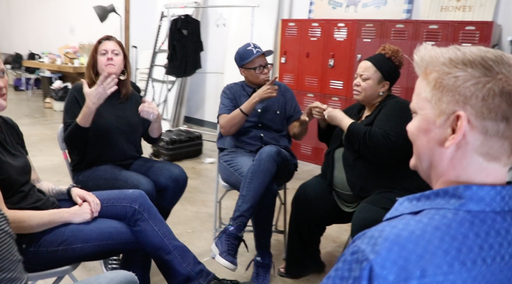 Diverse group of hearing, Deaf, and Deafblind people sitting in a circle talking with ASL, protactile sign language, and English