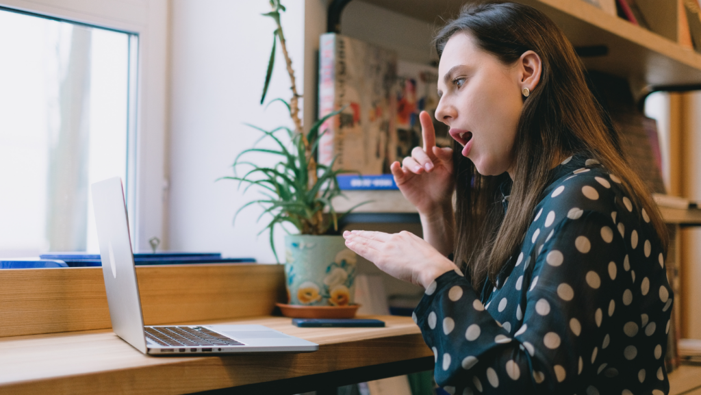 photo of a white woman seated at desk signing on a laptop in a green and white polka dot shirt