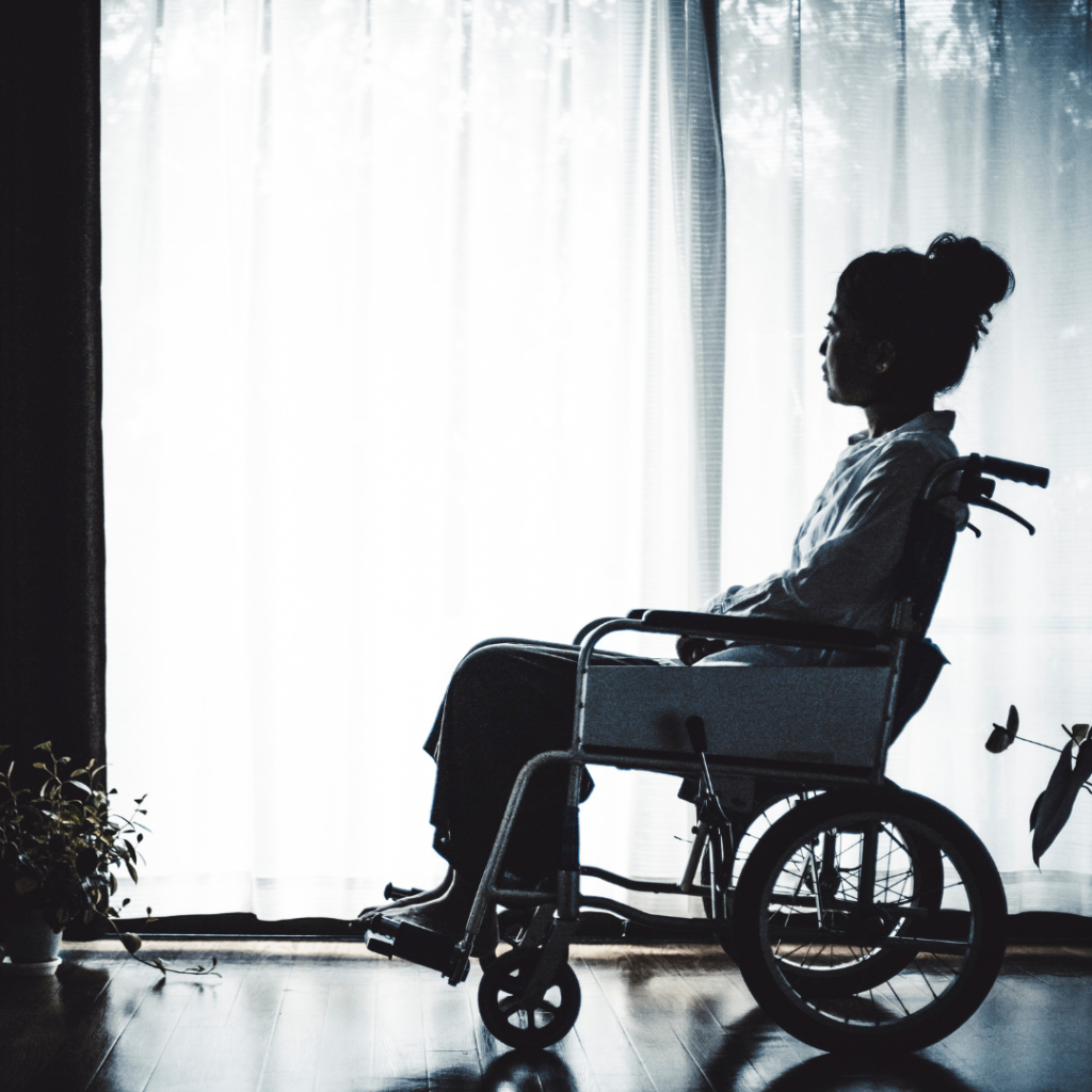 black and white photo of a woman sitting in a wheelchair looking out at a window