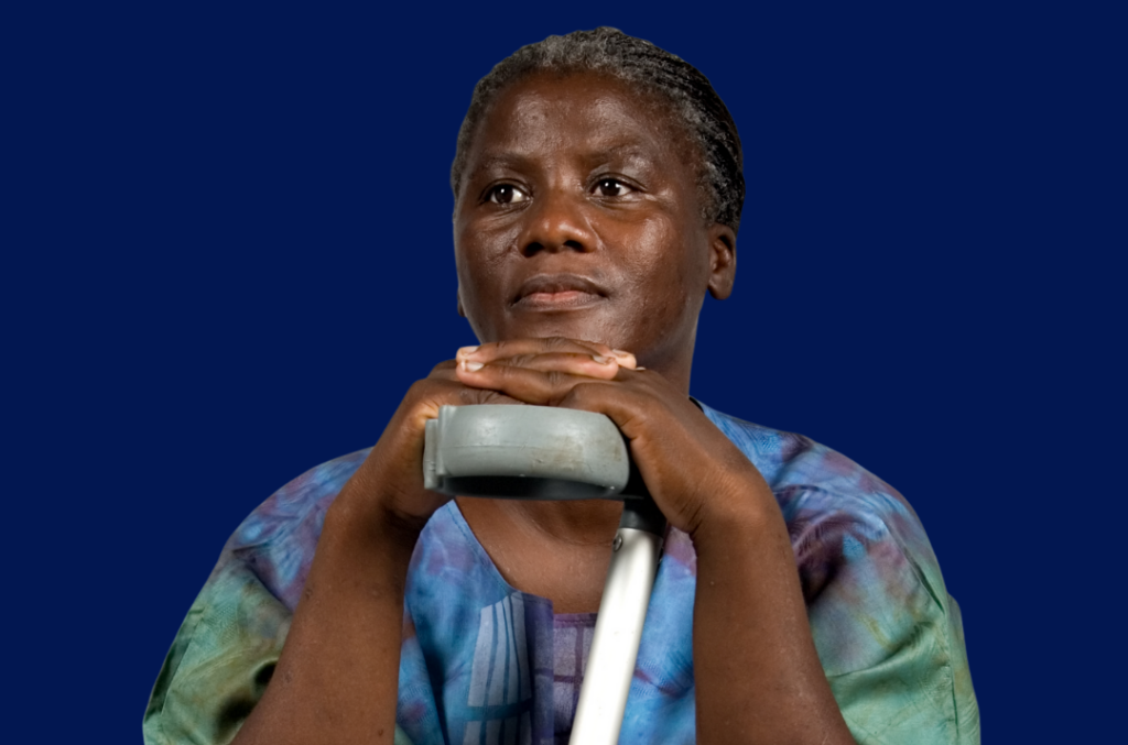 photo of an older Black woman with salt and pepper hair holding an arm brace/crutch while sitting down